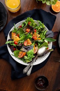 A vibrant salad featuring fresh greens, cherry tomatoes, and citrus slices in a white bowl, set on