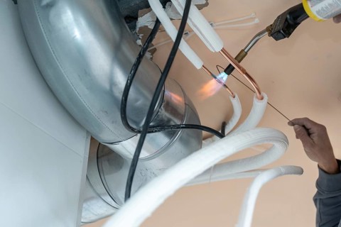 Technician installing a modern hvac system, using a blowtorch to braze copper pipes for an air