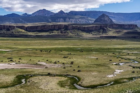 Meandering stream in wide grassland with basalt cliffs and volcanic mountain peaks in the