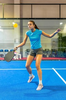 Woman playing pickleball on an indoor court, actively swinging a paddle to hit the ball,