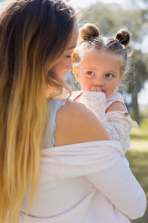 A pregnant woman lovingly holds her young daughter on a sunny day outside. They share a tender
