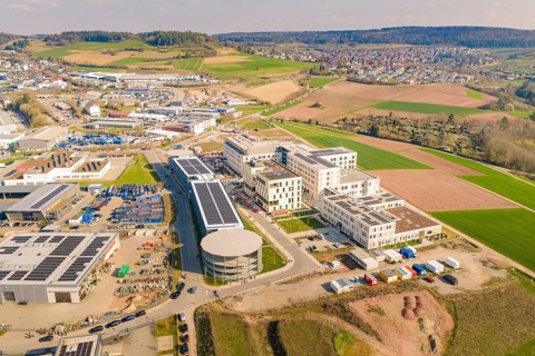 Industrial area with solar systems and modern buildings, surrounded by rural and urban landscape,