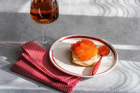 From above, a sumptuous display of red trout caviar atop a slice of bread, accompanied by a glass
