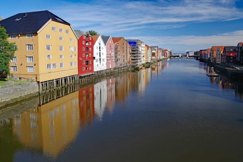 Colourful buildings reflected in the calm water of a river under a blue sky, Nidelva, Trondheim,