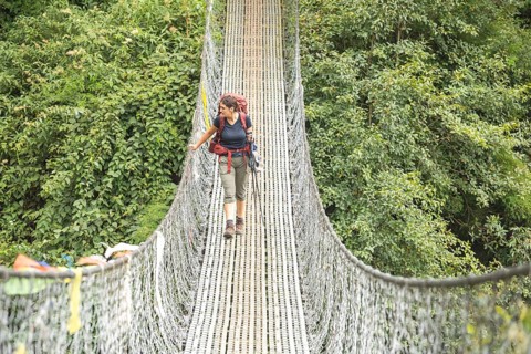 A woman treks across a suspension bridge surrounded by lush green foliage in the Everest region.