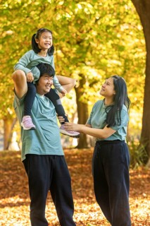Joyful Asian family in a park on a sunny autumn day. Child sitting on father's shoulders, while