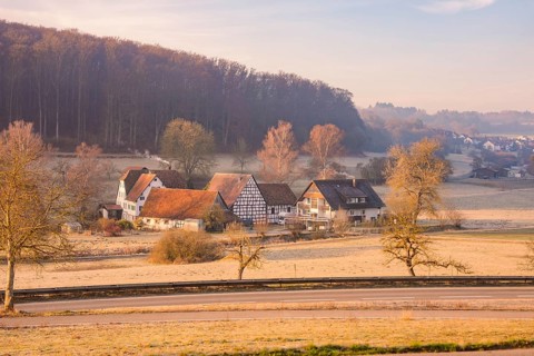 Idyllic village landscape with half-timbered houses and wooded hills in morning sunlight,
