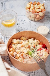 Caesar salad in a paper container, take it on the way, with sauce and croutons, on the table,