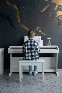 A young boy in casual attire sits on a bench, focused intently on playing a white electric piano in