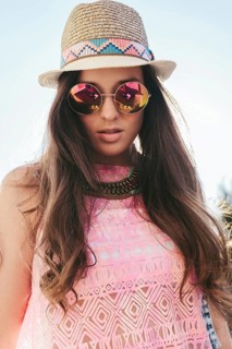 A young woman embodies summer style in a straw hat and stylish sunglasses. Her pink patterned top