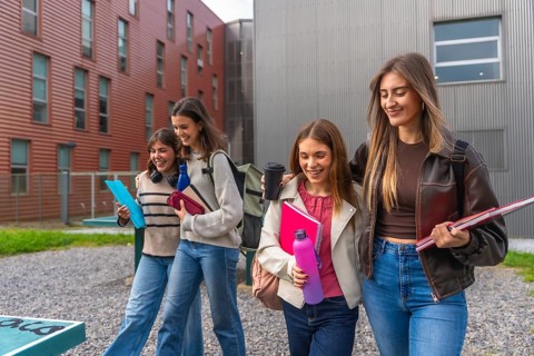 Diverse group of smiling female students walking and chatting on a university campus, carrying