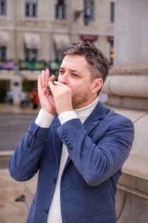 Man musician in a blue blazer and white sweater playing blues on a harmonica with eyes closed,