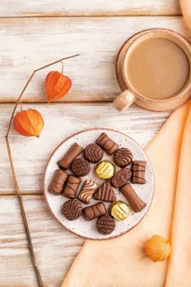 Chocolate candies with cup of coffee and physalis flowers on a white wooden background and orange