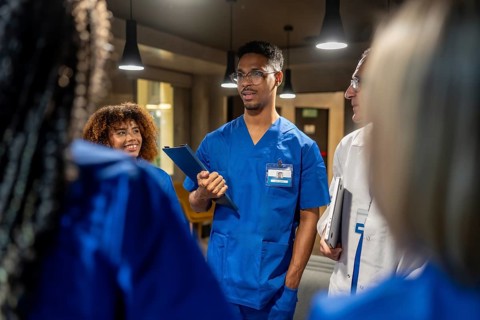 Healthcare team in scrubs and lab coats discussing patient care, sharing notes and a laptop,