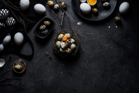 From above composition of raw chicken eggs on plates and quail eggs in nest on black background