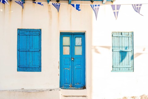 Sunlit Greek building facade featuring blue wooden doors and shutters in Plaka, Milos island. Greek