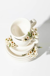 Top view of elegant white cups and plates, beautifully adorned with delicate spring flowers.