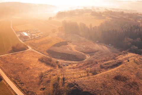 Wide, hilly landscape with fields and trees in soft morning light from the air, landfill,
