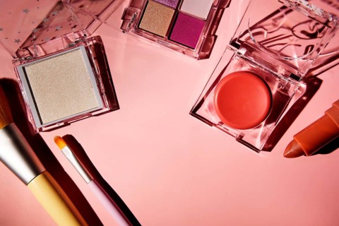 Top view of vibrant pink makeup set, including eyeshadow palette, blush, lipstick, and brushes,