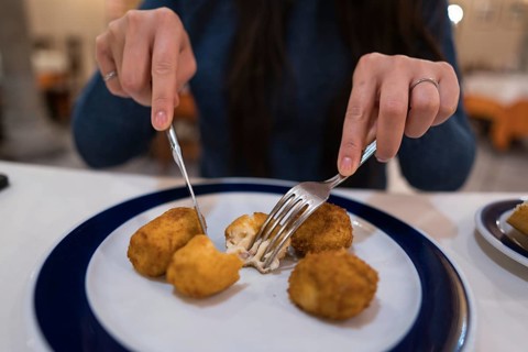 Woman enjoys a plate of croquetas at a rustic Spanish restaurant, surrounded by traditional decor