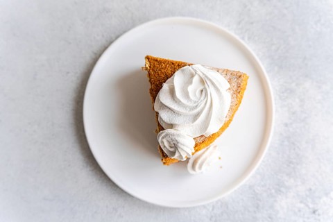 From above a slice of homemade honey cake topped with a swirl of vanilla zephyr sits elegantly on a