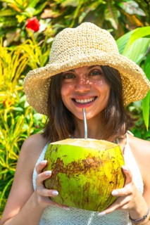 Young woman wearing straw hat enjoying fresh coconut water in tropical garden in siargao island,