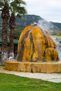 A hot spring with steaming rocks surrounded by palm trees and mountains, Karahayit Kirmizi Su, Red