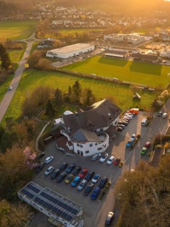 Aerial view of a rural area with buildings and car parks near a sports field at sunset,