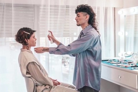 Professional makeup artist spraying a cosmetic product on a model's face, skillfully preparing her