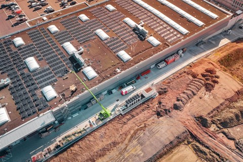 Aerial view of a commercial building with solar panels and adjacent construction site, PV Bau Auf