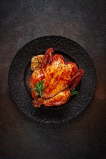 Baked chicken on a black dish with herbs and garlic, on a dark background, homemade, no people