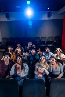 Group of excited friends wearing 3d glasses and eating popcorn while watching a movie in the cinema