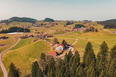 An idyllic alpine landscape with scattered buildings and green hills in clear weather, Oberreute,
