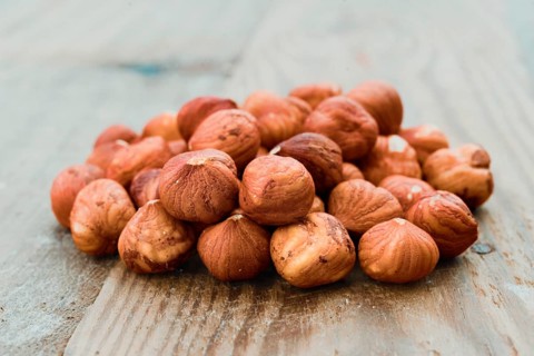 A close-up shot of a pile of fresh hazelnuts resting on a rustic wooden tabletop. The hazelnuts