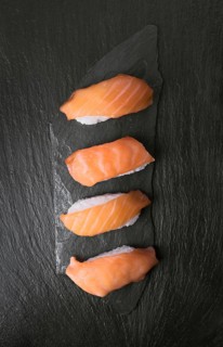 Four pieces of fresh salmon sushi arranged neatly on a textured black stone surface. The vibrant