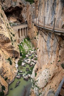 A path on a bridge leads over a rocky gorge with a river on the Caminito del Rey trail, Malaga