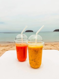 Two vibrant fruit smoothies sit on a table overlooking the serene, sandy beach in Phuket, Thailand.