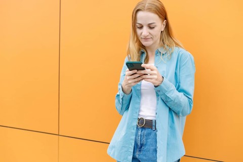 A woman in a casual blue shirt stands against a vibrant orange wall in Warsaw, focused on her