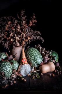 Autumn scene with green pumpkins, dried leaves, and a gnome statue on a rustic wooden table. The