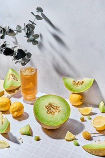 A vibrant display of fresh melons, lemons and fresh juice in a glass on a textured white