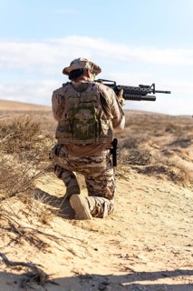 Soldier in full desert camouflage gear kneeling with firearm, ready for action. Training in open