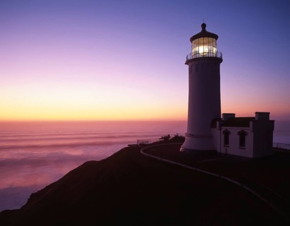 A picturesque view of Heceta North Head lighthouse illuminated by twilight against a vibrant sunset