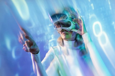 An elderly Asian woman wearing a virtual reality headset immerses herself in the metaverse. She