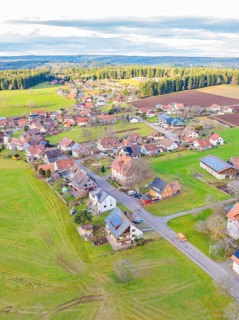 View from above of a small village with fields and houses in an open, green landscape with a cloudy