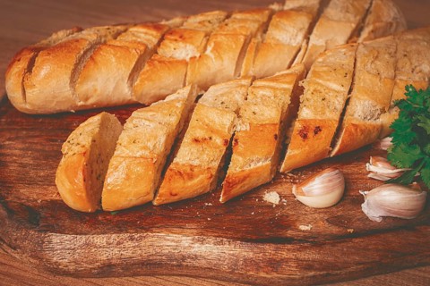 Garlic bread, baguette with garlic butter and herbs, on a wooden board, with herbs and garlic