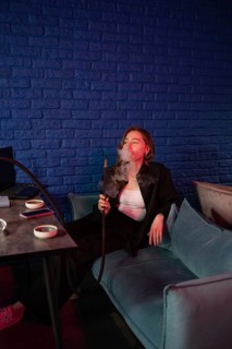 A woman enjoys a relaxed smoking session, sitting on a blue sofa with a hookah. The ambient red and