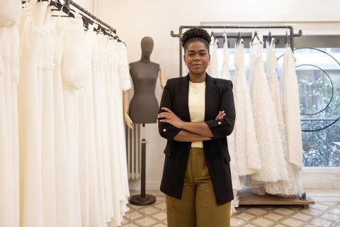 A confident fashion designer stands amidst elegant bridal gowns in a stylish atelier, exuding