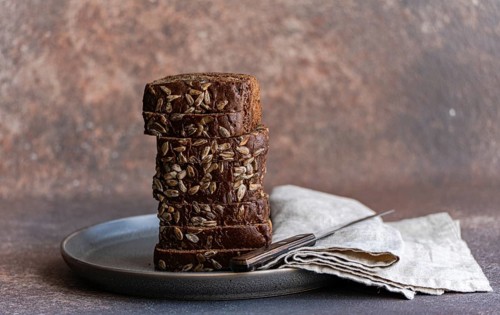 Slices of nutritious whole wheat bread adorned with sunflower seeds, stacked neatly on a dark