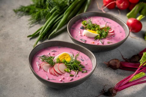 Two bowls of vibrant pink cold beetroot soup are garnished with sliced radishes, dill, green