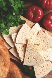 Georgian sliced cheese, on a wooden chopping board, with tomatoes with herbs and lavash, rustic